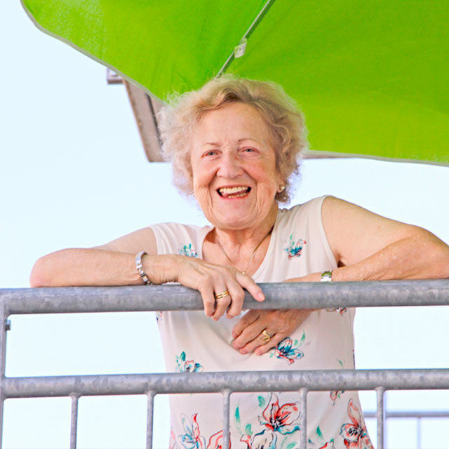 Bewohnerin lächelt fröhlich vom Balkon herunter